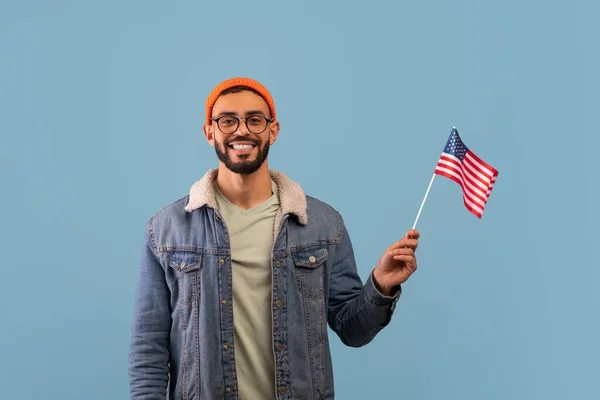 Garçon arabe positif tenant drapeau américain et souriant à la caméra, posant sur fond bleu studio, espace de copie — Photo