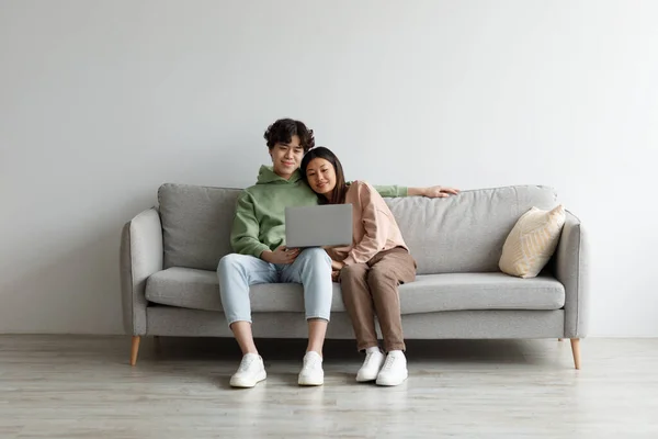 Afetuoso milenar ásia casal usando laptop computador, refrigeração juntos no sofá em casa, espaço livre — Fotografia de Stock
