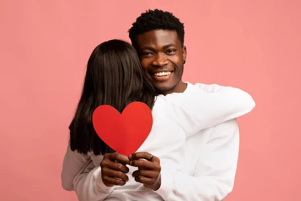 Felice uomo afro-americano abbracciare la sua ragazza, tenendo il cuore rosso — Foto Stock