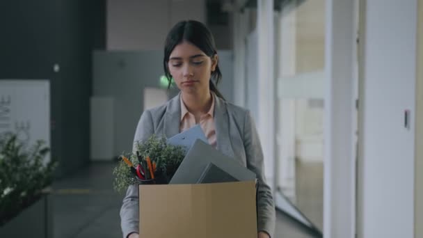 End of career. Young fired upset woman walking through office building, carrying box with personal belongings and crying — Stockvideo