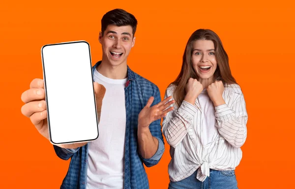 Возбужденная пара показывает белый пустой экран смартфона рядом с камерой — стоковое фото