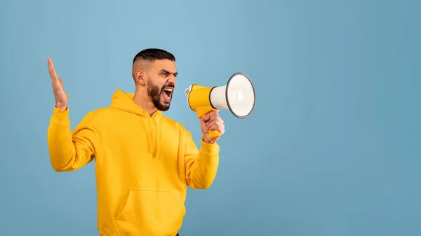 Učiním důležité oznámení. Rozzlobený mladý arabský muž křičí pomocí megafonu, modré pozadí, kopírovací prostor — Stock fotografie