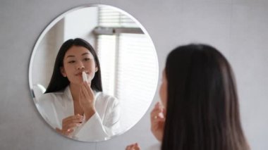 Banyoda aynaya bakarak ruj süren Asyalı genç bayan.