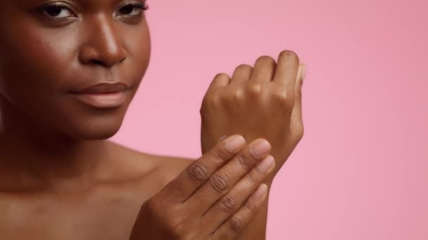 Femme noire appliquant crème hydratant sur la main sur fond rose — Video
