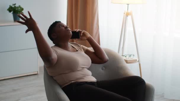 Невдоволена надмірна вага афроамериканська леді говорить на мобільному телефоні вдома — стокове відео