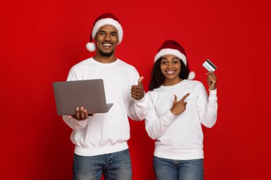 Bilgisayarı ve kredi kartı olan Noel Baba şapkalı mutlu çift.