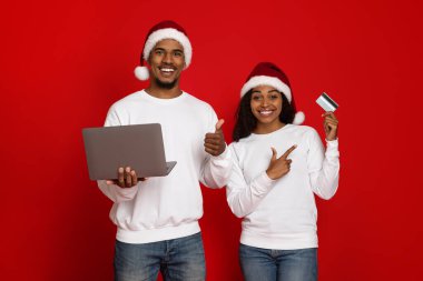 Bilgisayarı ve kredi kartı olan Noel Baba şapkalı mutlu çift.