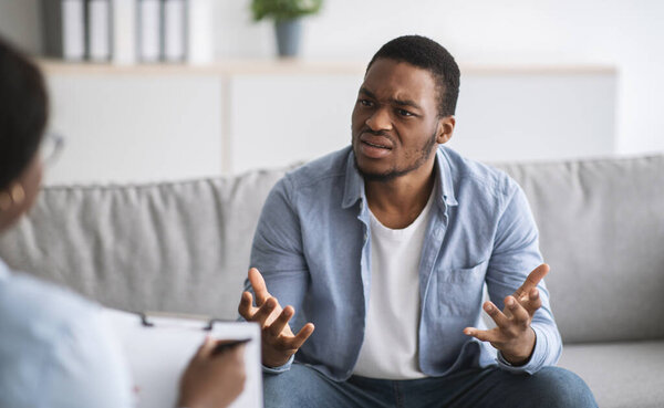 Psychologist helping depressed young black man, giving consultation to male patient at office