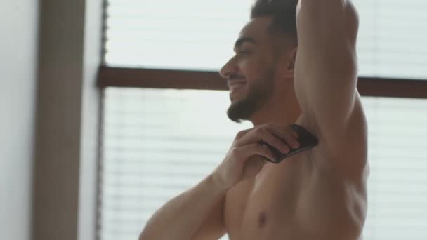 Koncepcja higieny. Widok z boku młody przystojny arabski mężczyzna bez koszuli stosując dezodorant na jego pachy w łazience rano — Wideo stockowe
