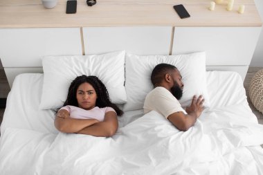 Offended young african american wife with crossed arms on chest, cant sleep with snoring husband on bed