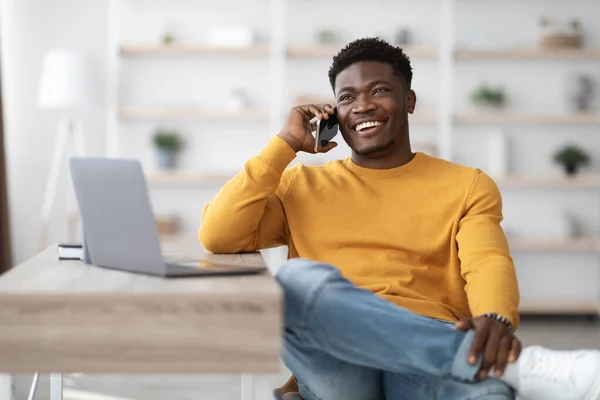 Cheerful man sitting at table with laptop, talking on phone — Foto Stock