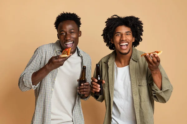 Mens Leisure Concept. Two Black Guys Holding Beer Bottles And Eating Pizza