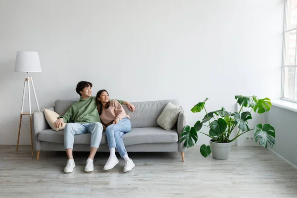 Spending weekend together. Happy millennial Asian couple resting on couch at home, empty space — Fotografia de Stock