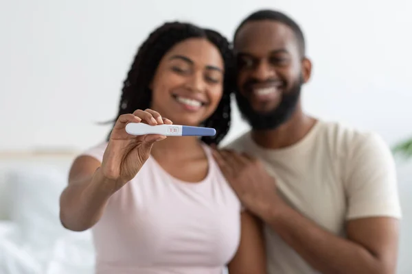 Satisfied smiling young african american woman and man with pregnancy test in white bedroom interior, selective focus — Stock fotografie