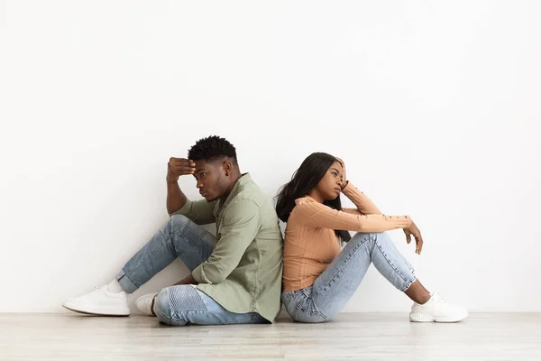 Upset african american couple sitting back to back on floor — Stockfoto