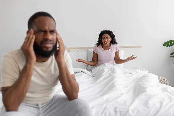 Mujer negra joven descontenta jura y le grita triste marido ofendido en la cama en el interior del dormitorio blanco —  Fotos de Stock