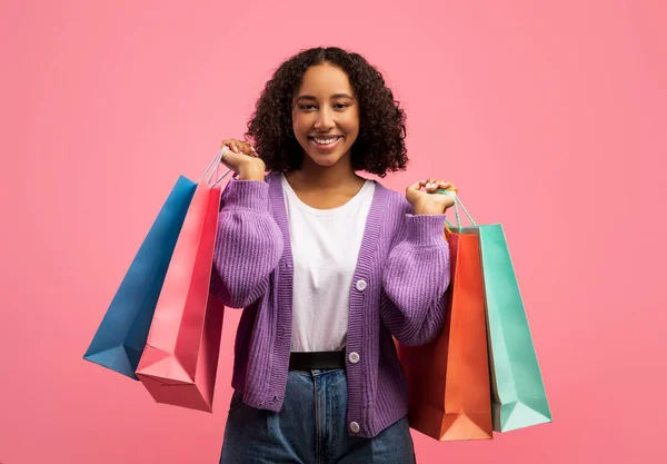 Encantadora joven mujer negra con bolsas de compras sonriendo a la cámara en el fondo del estudio rosa —  Fotos de Stock