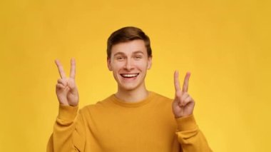 Cheerful Man Gesturing V-Sign Smiling To Camera Over Yellow Background
