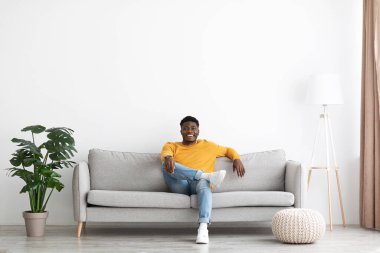Cheerful black guy in casual sitting on sofa at home