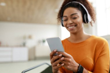Kablosuz kulaklıklı gülümseyen siyah kadın cep telefonu kullanıyor.
