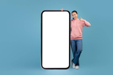 Pretty asian woman standing by huge smartphone with empty screen