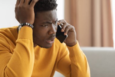 Puzzled african american guy having phone conversation