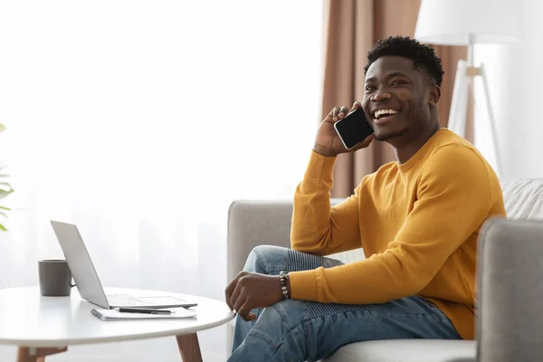 Positive black guy working from home, having phone conversation — Stock Fotó