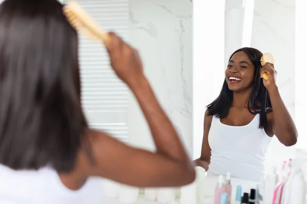 Beautiful African American Woman Combing Her Hair With Bamboo Brush In Bathroom — Stok Foto