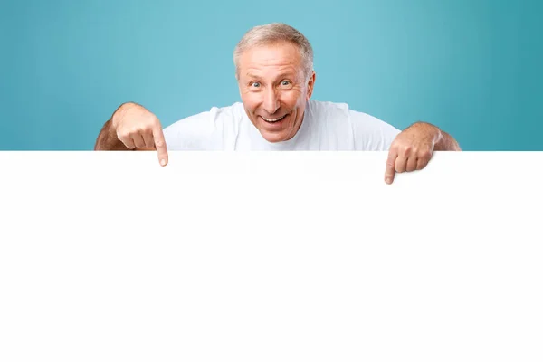 Mature man peeking out blank white advertising billboard at studio — Stock Photo, Image
