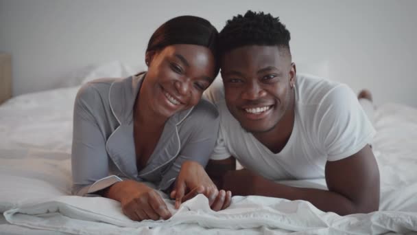 Zoom in portrait of young happy african american man and woman wearing pajamas lying in bed together and smiling — 비디오