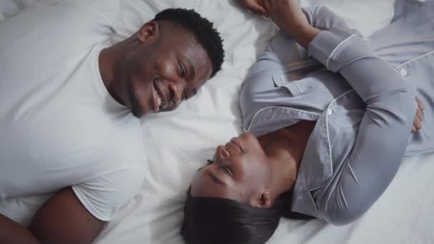 Honeymoon. Top view of young african american married man and woman lying in bed at looking at each other with love — Stockvideo