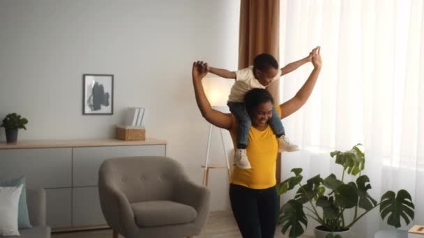 Black mom playing with little son at home, carrying him on neck — Stock video