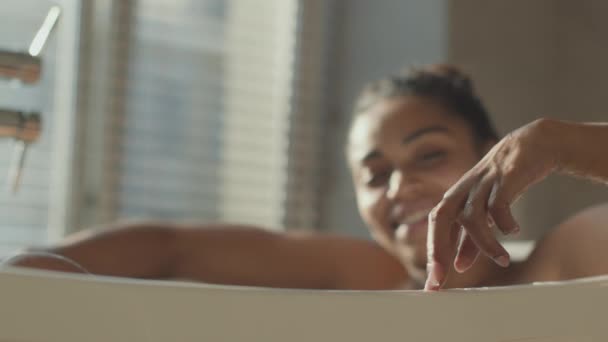 Home fun and relax. Playful african american lady stepping fingers on bathtub, taking bath at home, selective focus — стоковое видео