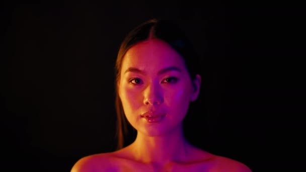 Hermosa mujer asiática girando cara a cámara y sonriendo bajo luces de neón — Vídeos de Stock