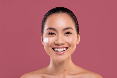 Yanağında nemlendirici kremi olan Asyalı genç bir kadın.