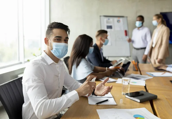 Seguridad en el trabajo. Empresario árabe usando máscara médica usando aerosol desinfectante en la oficina — Foto de Stock