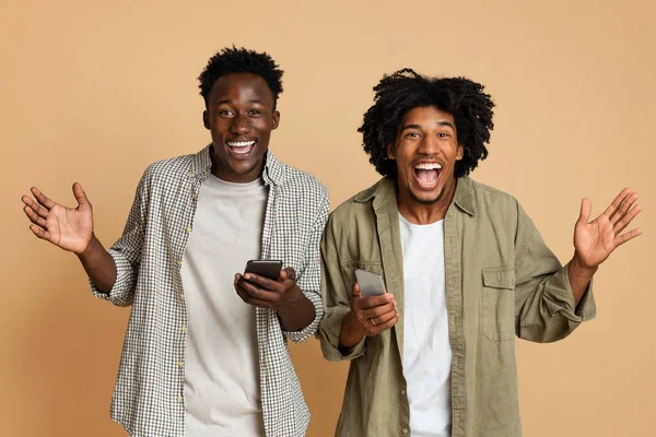 Mobile Offer. Portrait Of Two Excited Black Friends With Smartphones In Hands —  Fotos de Stock