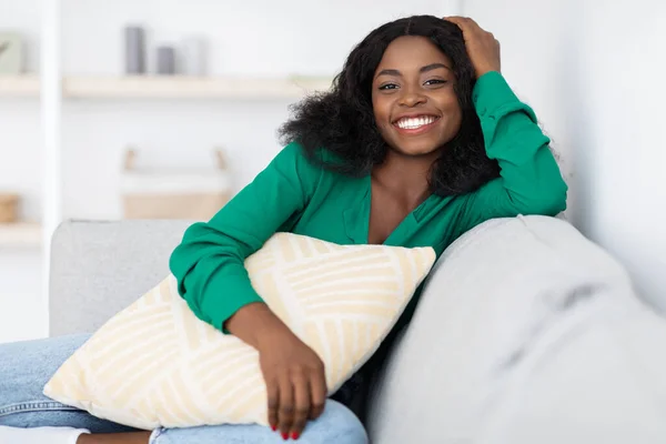 Smiling pretty african american woman sitting on couch at home — стоковое фото