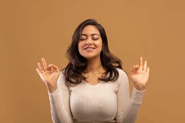 Meditation concept. Peaceful arab woman making om gesture and meditating with eyes closed, beige background — Fotografia de Stock