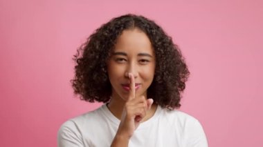African American Woman Gesturing Finger On Lips Over Pink Background