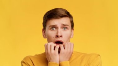 Scared Guy Biting Nails Looking At Camera Over Yellow Background