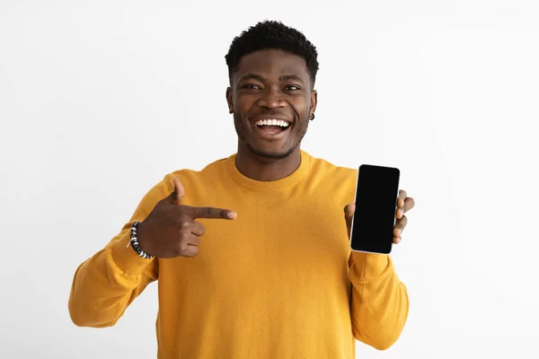 Laughing african american guy in casual pointing at smartphone, mockup — 스톡 사진