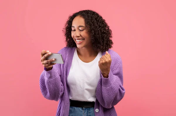즐거운 젊은 흑인 여성 스마트폰 화면을 보면서 핑크 녹음실 배경 에서 YES 제스처를 하는 모습 — 스톡 사진