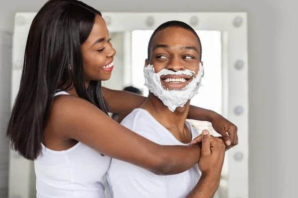 Alegre negro pareja abrazando en cuarto de baño mientras hacer belleza rutina en casa — Foto de Stock