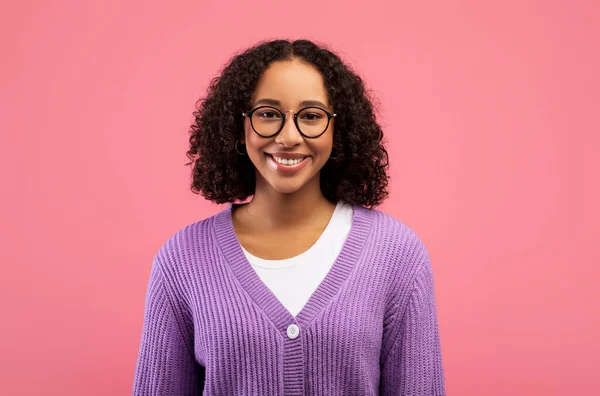 Feliz joven afroamericana mujer con hermosa sonrisa y pelo rizado mirando a la cámara, posando sobre fondo rosa — Foto de Stock