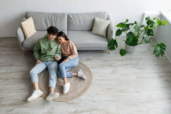 Cheery Asian couple using smartphone application, relaxing on sofa at home on weekend, top view. Copy space — Fotografia de Stock
