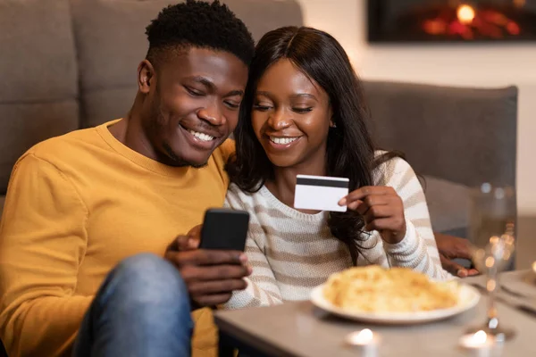 Black Couple ช้อปปิ้งออนไลน์บนสมาร์ทโฟนโฮลดิ้งบัตรเครดิตในร่ม — ภาพถ่ายสต็อก