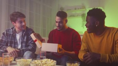 Best gift from bros. Multiethnic guys greeting their friend, middle eastern guy opening box, laughing together at home