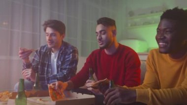 Friday evening fun. Zoom in of three multiethnic guys friends enjoying pizza and beer, watching tv show together at home