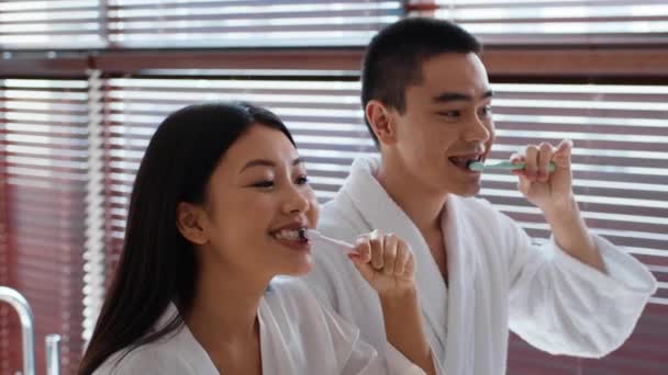 Cheerful Japanese Couple Brushing Teeth With Toothbrush In Modern Bathroom — стоковое видео